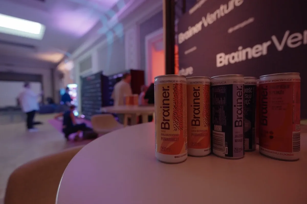 Cztery puszki Brainera na stoliku, w tle ścianka Brainer Venture i sala festiwalowa